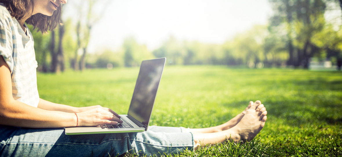 Tjej sitter med laptop på gräsmatta.